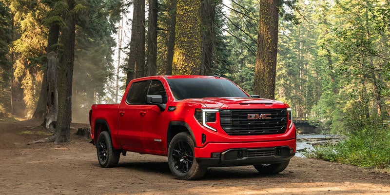 Red GMC Sierra 1500 parked on a dirt trail in a forest setting